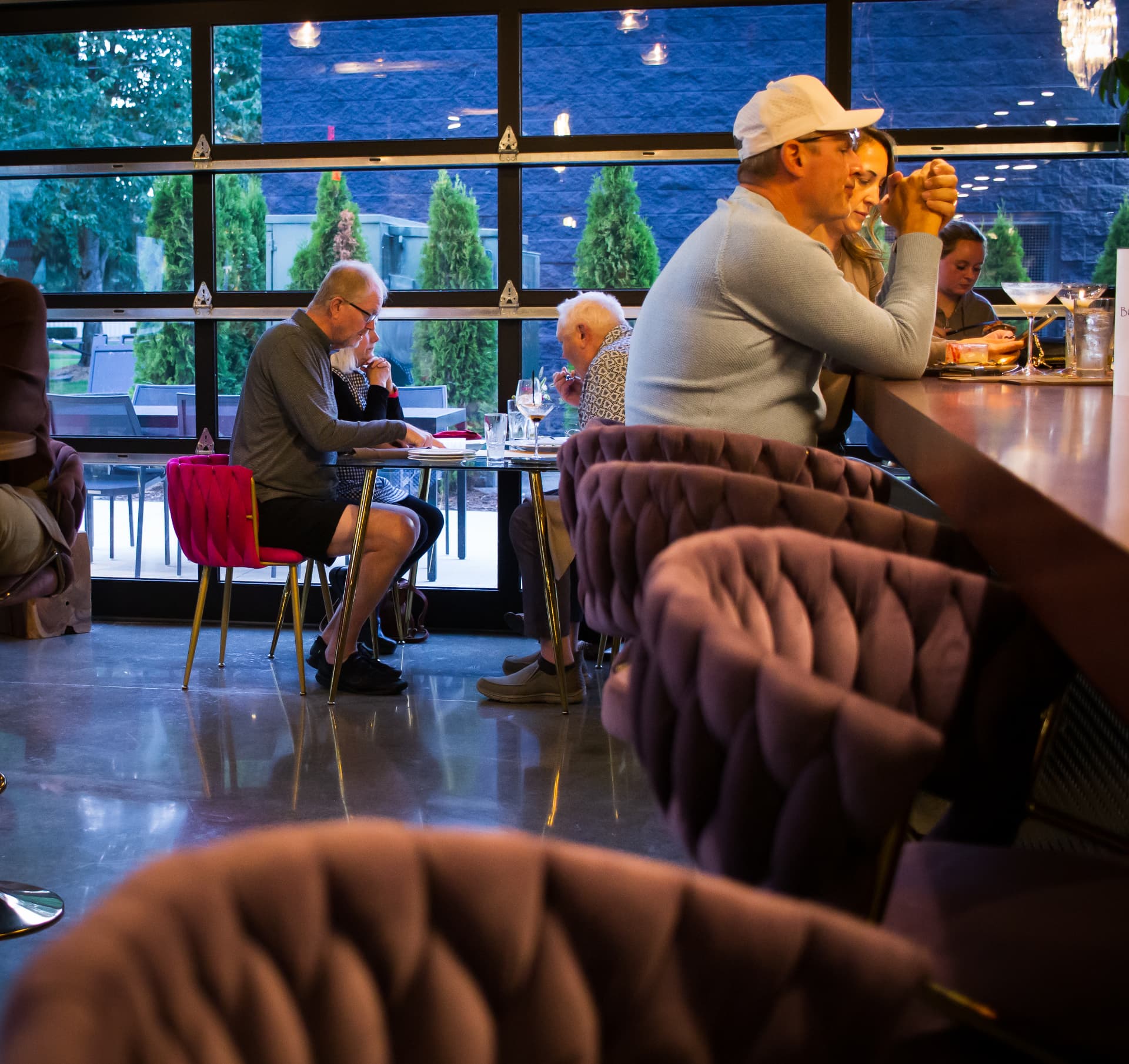 Guests dining in velvet chairs beside the glass garage doors at Bottega